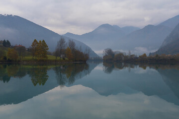 Fototapeta na wymiar Foggy Alps mountains reflection in a calm lake on a cloudy autumn day