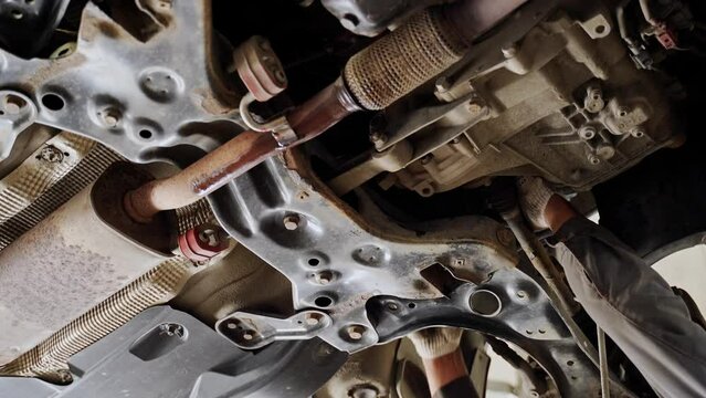 the hands of the master work under the car raised on the lift. view of the gearbox, suspension, subframe, levers, traction, muffler
