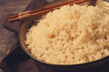 A plate of boiled rice, with wooden sticks, on a brown background, no people, selective focus, toned.