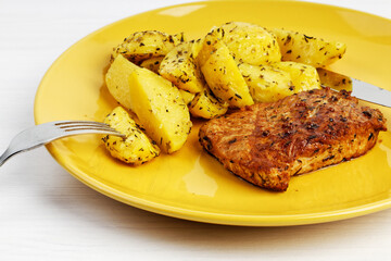 Closeup grilled turkey steak with a garnish of baked potatoes in a yellow plate on white wooden table.