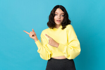 Fototapeta premium Teenager Ukrainian girl isolated on blue background frightened and pointing to the side