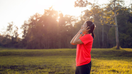 Asian sporty young woman closing their eyes to relax ,hold and using headphone listen music after exercise in the garden with copy space. Concept of sport technology to enjoy and entertainment.