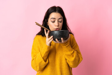 Young caucasian woman isolated on pink background holding a bowl of noodles with chopsticks and...