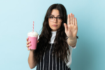 Young woman with strawberry milkshake isolated on blue background making stop gesture