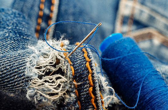 Hole in jeans. Needle with thread for darning jeans. Tools for work dressmaker, seamstress fashion designer