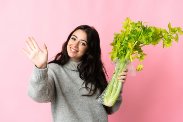 Young caucasian woman holding a celery isolated on blue background saluting with hand with happy expression