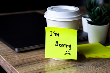 Handwritten note I'm sorry on the a cup of coffee set next to laptop on the working desk in office,...