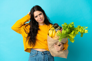 Young woman holding a grocery shopping bag isolated on blue background having doubts