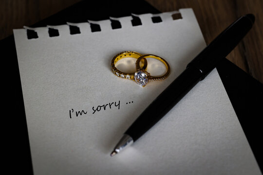 Text "I am sorry"  with wedding ring, engage ring on white note with a pen, message for ending relationship or break up. Lovesick and breaking up or divorce concept.