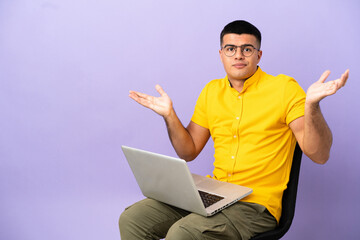 Young man sitting on a chair with laptop having doubts while raising hands