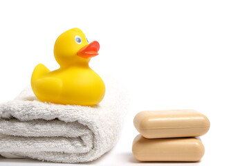Yellow rubber duckling on white terry towel and two pieces soap.