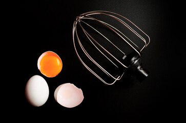 whisk for whipping and broken eggs in the shell on a black background