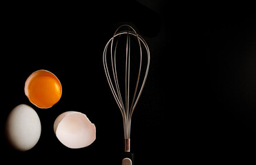 whisk for whipping and broken eggs in the shell on a black background