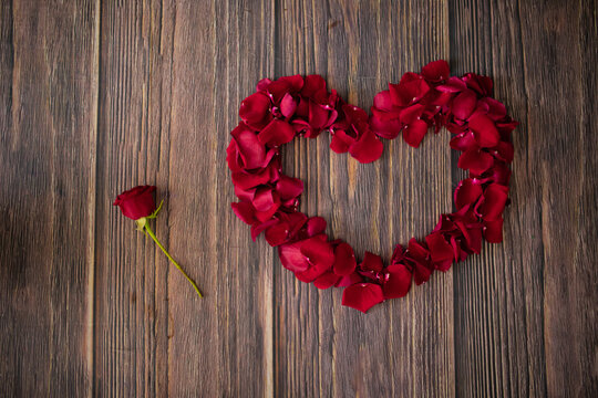 beautiful photo of a heart made of red rose petals and next to it lies another small red rose on a wooden floor, surprise for valentine's day, date, love