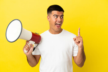 Young handsome man over isolated yellow background holding a megaphone and intending to realizes the solution