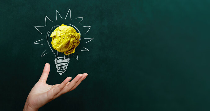 hand holding yellow crumpled paper ball with Light bulb  doodle on blackboard background innovation idea concept.