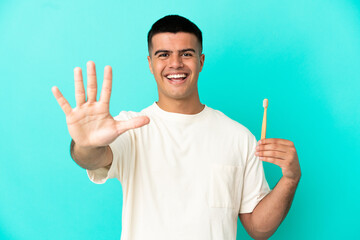 Naklejka premium Young handsome man brushing teeth over isolated blue background counting five with fingers