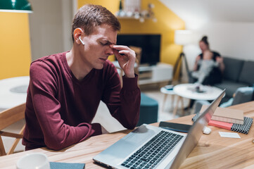 Redhead man having a headache while using a laptop at home.
