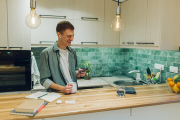 Redhead man using a smartphone while drinking coffee in the kitchen