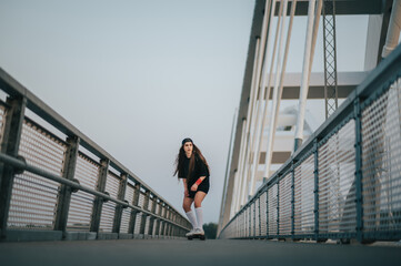 Young woman riding her longboard on the bridge