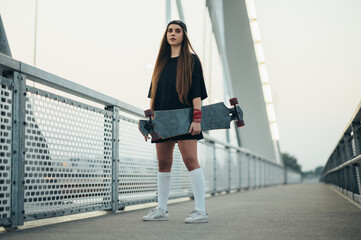 Obraz premium Young woman holding her longboard and standing on the bridge