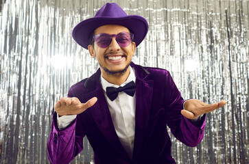 Cheerful young guy dressed in original purple corduroy tuxedo having fun on silver background....