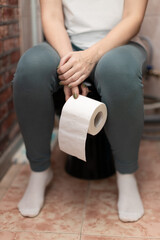 woman sitting on the toilet holding a roll of paper