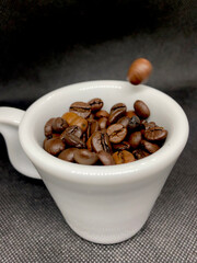 Coffee bean falling into a cup of coffee closeup view with selective focus on foreground