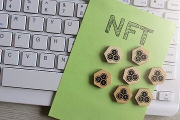 Top view image of keyboard, paper with text NFT and wooden hexagon with cryptocurrency icon.
