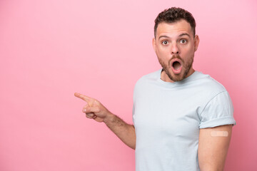 Young Brazilian man wearing a band-aids isolated on pink background surprised and pointing side