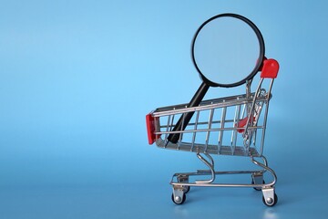 Magnifying glass inside shopping cart. Blue background. Product search and frugal shopping concept.
