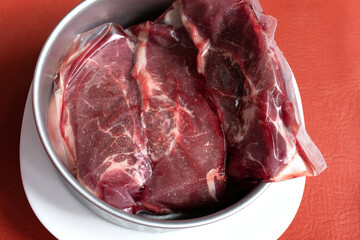 Frozen raw piece of meat in a bowl on a red background. thawing, raw ready to cook.