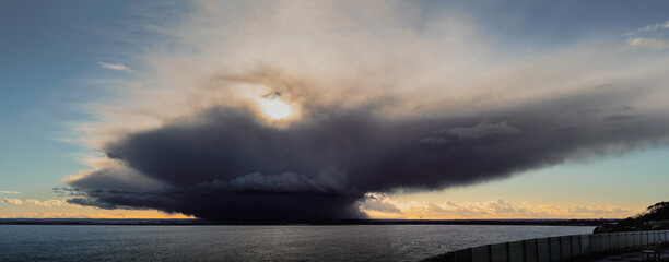 A dramatic panoramic image of a rain cloud on the horizon above the sea and a peninsula