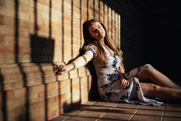 Fototapeta na wymiar Caucasian woman sitting on floor leaning against brick wall and smiling at camera