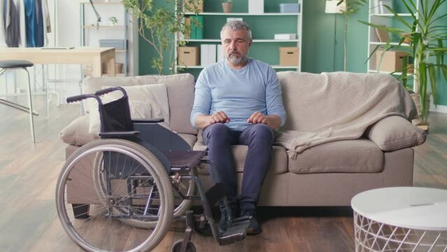 A Lonely Senior Man with a Disability Sitting on the Couch, Feeling Lonely, Depressed, Thinking About the Illness. Psychological Health, Nostalgia, Aging, Isolation. Nursing Home Concept.