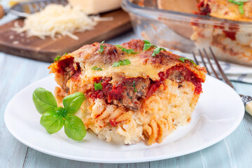 Mac and cheese with meatballs, mozzarella, tomato sauce and basil, on white plate, horizontal