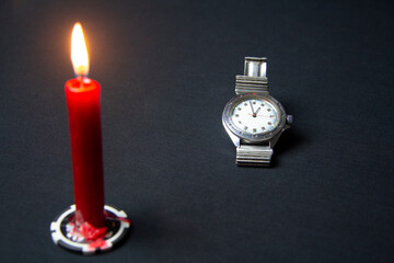 A wristwatch and a red candle on a black background