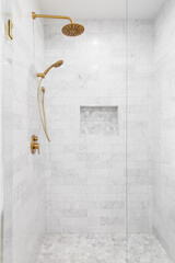 A luxury shower with a gold faucet and shower head, marble subway tile walls, and marble hexagon...