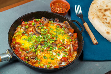 Shakshuka in a frying pan on a gray background next to a fork on a blue napkin.