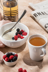 Oatmeal porridge with fresh berries in a ceramic bowl with tea and newspaper
