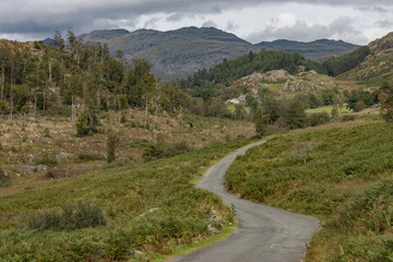 Fototapeta na wymiar Country road in the Lake District, close to Seathwaite, winds its way through the upland hills and vegetation with Ulpha Fell and Cold Pike in the distance