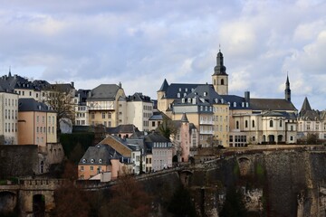 Fototapeta na wymiar Tower of Saint Michael's Church seen over some buildings of Luxembourg old town. View over Alzette river valley on early spring day