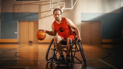Fototapeta premium Portrait of Handsome Wheelchair Basketball Player Wearing Red Shirt Dribbling Ball, Looking at Camera and Smiling. Determined Person with Disability who is Gonna Win and be Champion