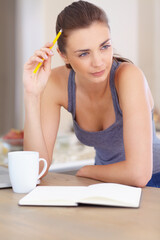 Writers block. A beautiful young woman looking thoughtful while writing in a book.