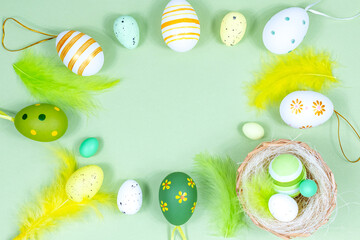 Easter frame with eggs, feathers and a nest on a green background. Minimal concept. View from above. Card with copy space for text.