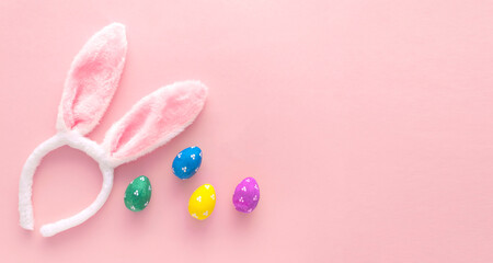 Decorated Easter eggs and bunny ears on color pink background, top view