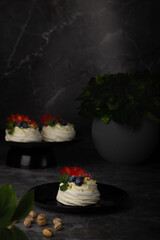 Selection of Pavlova desserts showcased against a grey backdrop, each topped with a mix of fruits and paired with dark tableware.