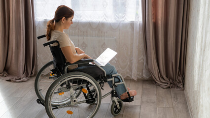 Fototapeta na wymiar Caucasian woman in a wheelchair typing with a laptop from home. Remote work for people with disabilities.