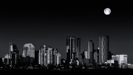 Black and white cityscape. Last full moon of 2021 setting over the Calgary Alberta city skyline lit...