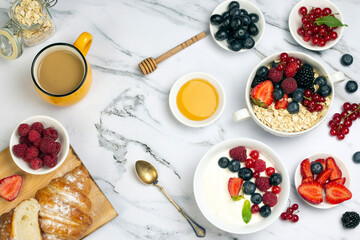 Healthy breakfast with cup of coffee, yogurt of fruit, oat with berry, honey and ripe sweet berries on white marble background top wave, flat lay.